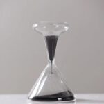 An hourglass with black sand flowing through a clear glass frame, used for measuring time in science experiments and educational activities.
