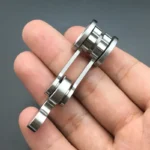 A close-up of a small metallic gear mechanism held between fingers, showcasing precision engineering and intricate design.