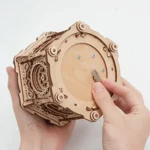 Hand holding a wooden mechanical puzzle box with gears and rotating parts, demonstrating a DIY science educational toy for kids and adults.
