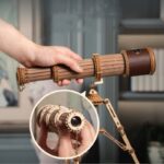 Hand holding a wooden and metal toy telescope with a tripod, designed for educational and science decor purposes.