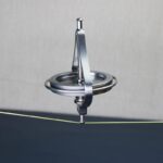 A metallic magnetic pendulum swinging over a circular metal plate, demonstrating magnetic forces and oscillation principles.