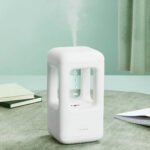 Modern white steam humidifier with open design, emitting visible steam, placed on a table in a cozy room setting.