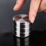Close-up of a person's finger balancing a shiny metal disc on a stack of similar discs, demonstrating magnetic properties and scientific principles.