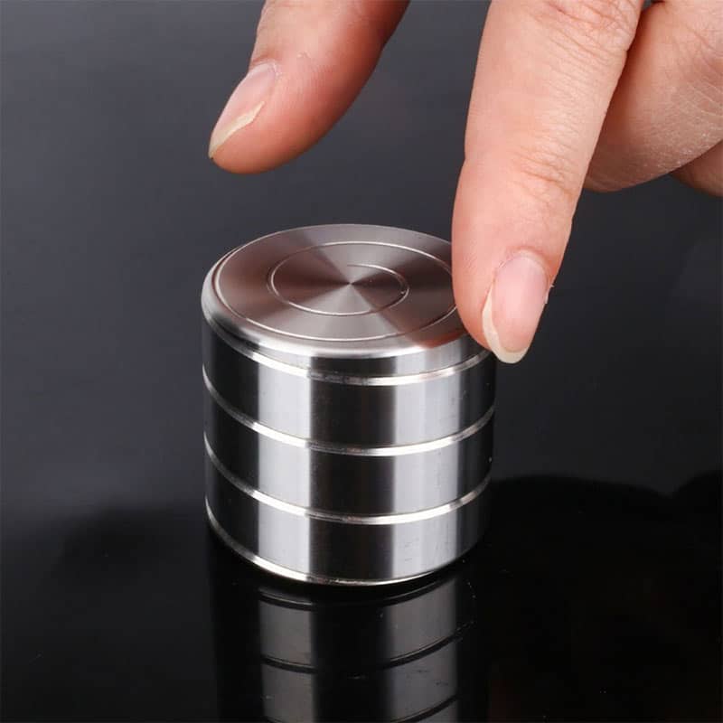 Close-up of a person's finger balancing a shiny metal disc on a stack of similar discs, demonstrating magnetic properties and scientific principles.