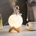 Astronaut lamp featuring a small astronaut figure sitting on a glowing moon-shaped light, with a star-shaped hanging ornament, ideal for science decor and educational toys.