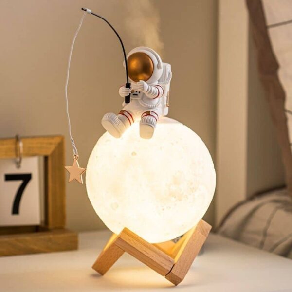 Astronaut figurine sitting on a moon-shaped lamp, holding a fishing rod with a star, creating a whimsical space scene.