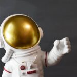 Astronaut figure with a shiny gold helmet and white spacesuit, giving a thumbs-up gesture.