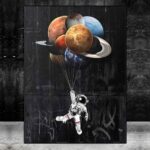 Astronaut floating in space holding planets as balloons, with a black background and graffiti art on the wall behind.