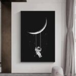 Artistic black and white wall art featuring a crescent moon and an astronaut hanging from a string, perfect for space enthusiasts and modern interior decor.