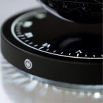 Close-up of a modern black scientific clock with illuminated white markings and a power button, showcasing precise time measurement and sleek design.