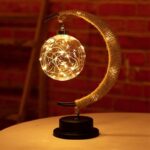 A decorative table lamp featuring a spherical bulb filled with string lights, attached to a curved, textured arm, creating a warm and inviting glow.