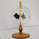 Small Tesla coil model demonstrating electrostatic principles with a glass sphere, metal electrodes, and a wooden base, used for educational science demonstrations.