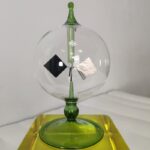 A glass globe with internal metallic components and a green base, designed as a decorative science gadget.