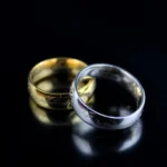 Silver and gold wedding rings with engraved patterns on a reflective black surface, symbolizing love and commitment.