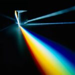 A glass prism disperses white light into a spectrum of colors, creating a vivid rainbow effect on a dark background.
