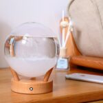 Modern air purifier with a glass water tank and wooden base, placed on a wooden surface in a cozy room setting.