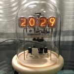 A vintage-style nixie tube clock displaying the year 2029 inside a glass dome. The clock features glowing numerals and intricate electronic components, combining retro aesthetics with modern craftsman.
