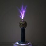 A Tesla coil producing purple lightning sparks with a reflective metallic sphere on top, demonstrating high-voltage electrical discharge.