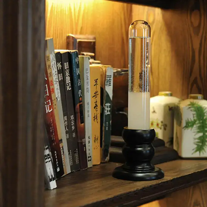 A magnetic levitation science toy displayed on a wooden bookshelf, featuring a clear glass tube with floating particles held above a black base, surrounded by books and decorative items.