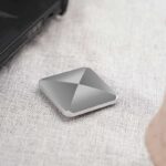 Small, sleek, silver Bluetooth tracker device placed on a textured fabric surface, used for locating gadgets and personal items easily.