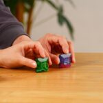 Green and purple galaxy-themed science dice held by hands on wooden surface.