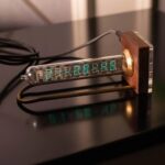 Vintage-style digital clock with a glass tube display showing the time 21:28:45, mounted on a wooden base with metallic accents, ideal for science-themed decor.