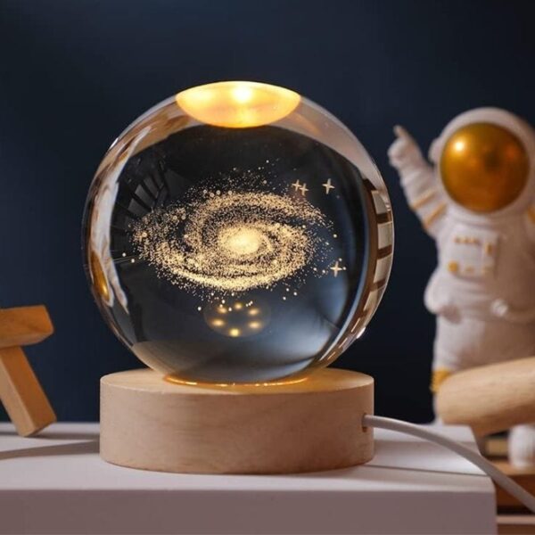 A glass sphere showcasing a detailed galaxy with stars and cosmic dust, mounted on a wooden base, perfect for science decor and educational displays.