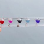 Brightly colored liquid drops suspended on a transparent tube, demonstrating fluid dynamics and surface tension for educational purposes.