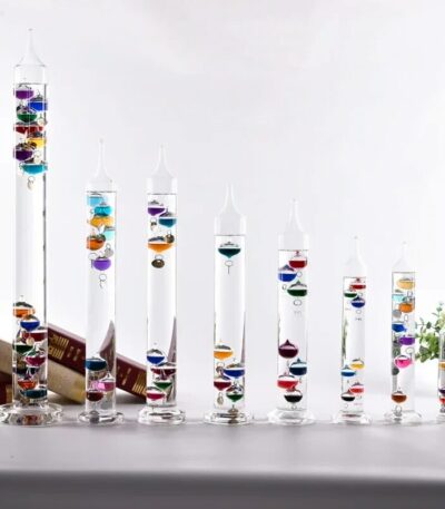 Set of eight transparent glass test tubes filled with colorful layered liquids, arranged from tallest to shortest on a white surface.