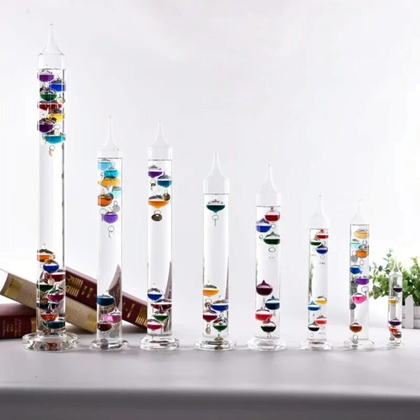 Set of eight transparent glass test tubes filled with colorful layered liquids, arranged from tallest to shortest on a white surface.