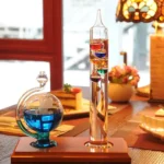Glass science experiment apparatus with colorful liquids and floating objects, displayed on a wooden table in a cozy indoor setting.