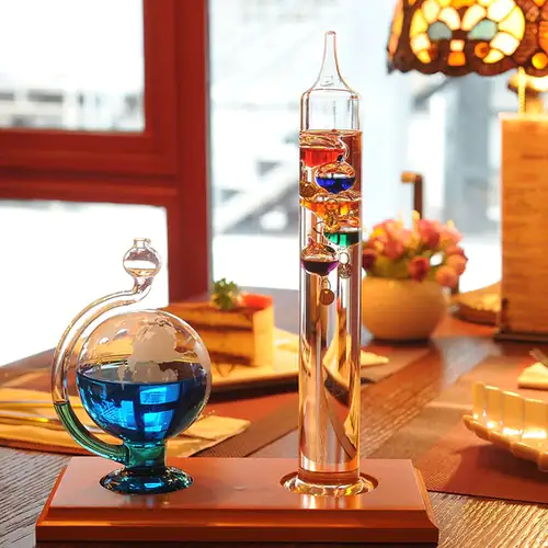 Glass science experiment apparatus with colorful liquids and floating objects, displayed on a wooden table in a cozy indoor setting.
