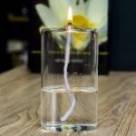 A glass of water with a floating candle wick and a lit matchstick at the top, demonstrating a simple science experiment with fire and water.
