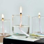A close-up of a candle wick submerged in water, with a visible flame, demonstrating scientific principles of combustion and water displacement.