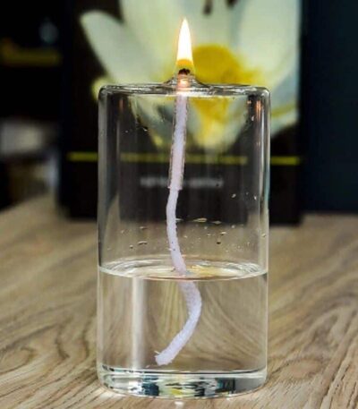 A glass of water with a floating candle wick and a lit matchstick at the top, demonstrating a simple science experiment with fire and water.