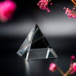 Clear glass pyramid ornament on black background with pink flowers, ideal for science-themed decor and educational purposes.