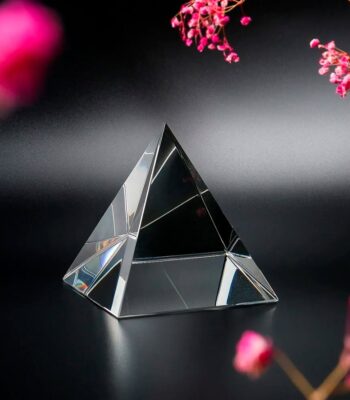 Clear glass pyramid ornament on black background with pink flowers, ideal for science-themed decor and educational purposes.