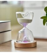 Modern glass hourglass timer with white sand, placed on a wooden base, used for time measurement or decorative purposes in science and educational settings.