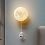 Moon-shaped night light with astronaut toy hanging below, creating a celestial decor piece for a child's room or science-themed space.