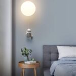 A whimsical robot-themed wall lamp resembling a small robot holding a glowing moon, perfect for adding a playful touch to a child's bedroom or nursery.