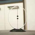 A magnetic pendulum science toy with a circular metal frame, two black balls, and a magnetic base, demonstrating physics principles.