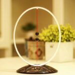 A modern magnetic levitating pendulum clock with a circular frame and two black balls suspended by magnetic forces, set on a sleek black base.