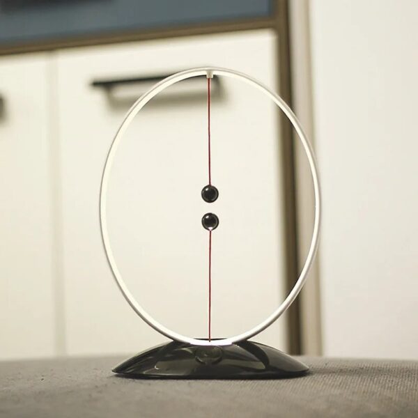 A magnetic pendulum science toy with a circular metal frame, two black balls, and a magnetic base, demonstrating physics principles.