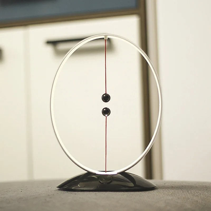 Magnetic Pendulum Science Toy A magnetic pendulum science toy with a circular metal frame, two black balls, and a magnetic base, demonstrating physics principles.