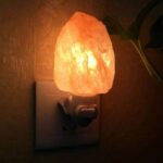 Warm Himalayan salt night light plugged into an electrical outlet, emitting a soft orange glow, perfect for creating a cozy atmosphere in any room.