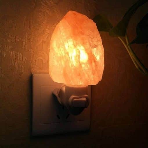 Warm Himalayan salt night light plugged into an electrical outlet, emitting a soft orange glow, perfect for creating a cozy atmosphere in any room.