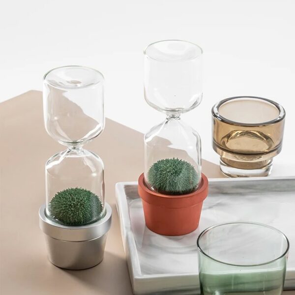 Glass hourglass with green moss in small pots, decorative science-themed items for home or classroom.