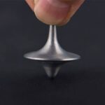 Close-up of a metallic spinning top being balanced on a finger, demonstrating magnetic levitation and rotational motion.