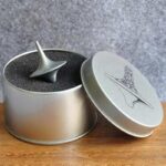 Metal spinning top toy inside a round tin container with foam padding, designed for educational and science demonstration purposes.