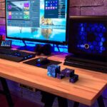 An advanced computer workstation featuring a large monitor displaying a digital interface, a gaming keyboard, mouse, and a high-performance desktop tower with blue LED lighting. Space-themed decorativ.